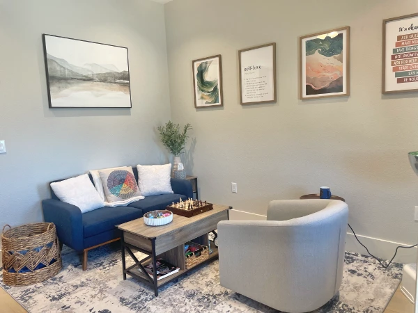 A stylish office room with modern decor, featuring a blue couch, armchair, and framed artwork on the walls.