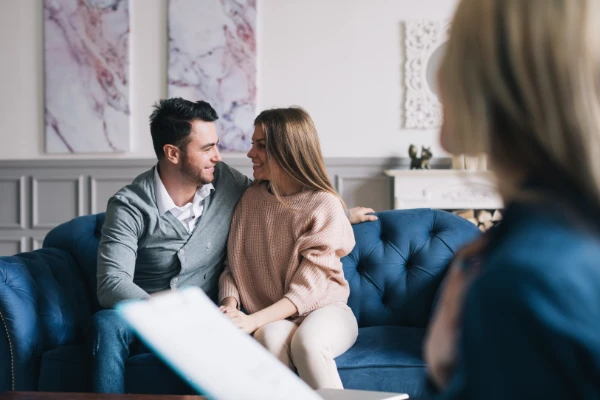 A happy couple sitting close together on a couch, engaged in a heartfelt conversation with soft smiles.