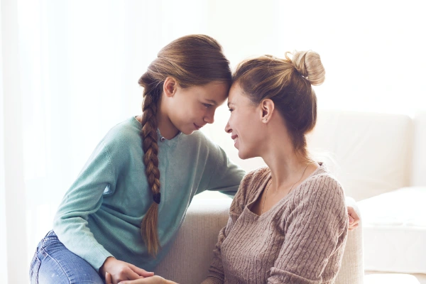 A mother and daughter sitting together, heads gently touching, sharing an intimate and loving moment.