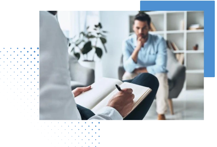 A therapist taking notes while a man sits in the background, deep in thought during a counseling session.