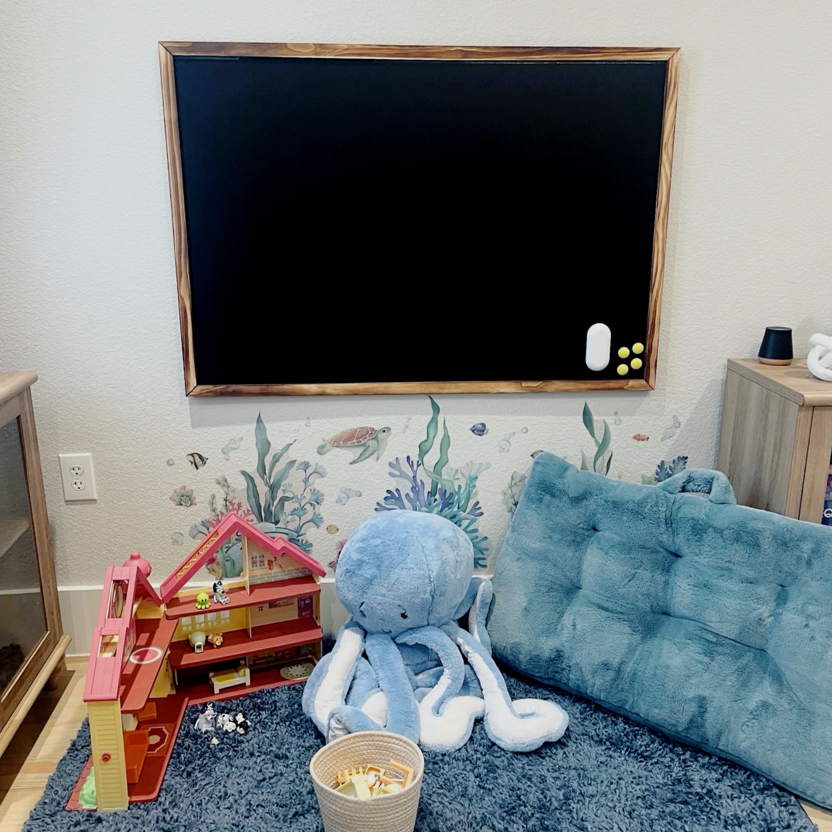 A cozy children's play area with a chalkboard, colorful toys, and a plush octopus on a fluffy rug.