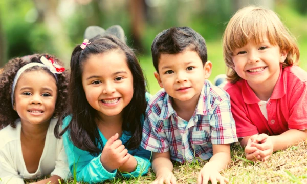 Four young children, sitting on the grass, smiling at the camera.