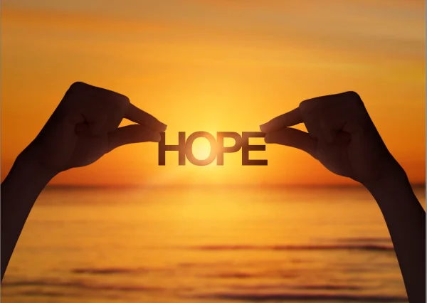 Hands holding the word "HOPE" against the backdrop of a sunset over the ocean.