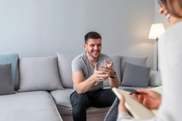 A man smiling while sitting on a couch, as he speaks with a counselor.