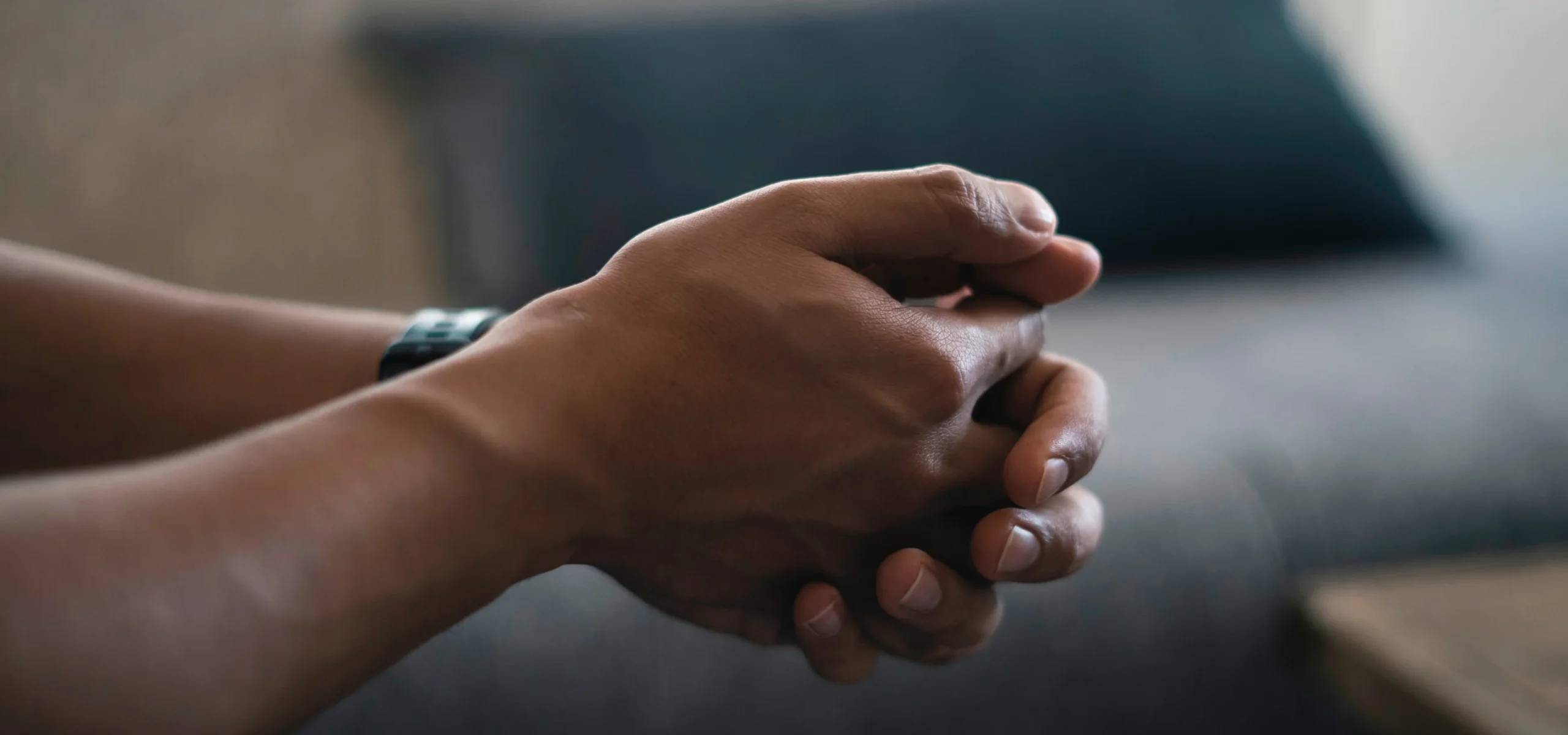 A close-up of a man's hands clasped together, resting on his lap.