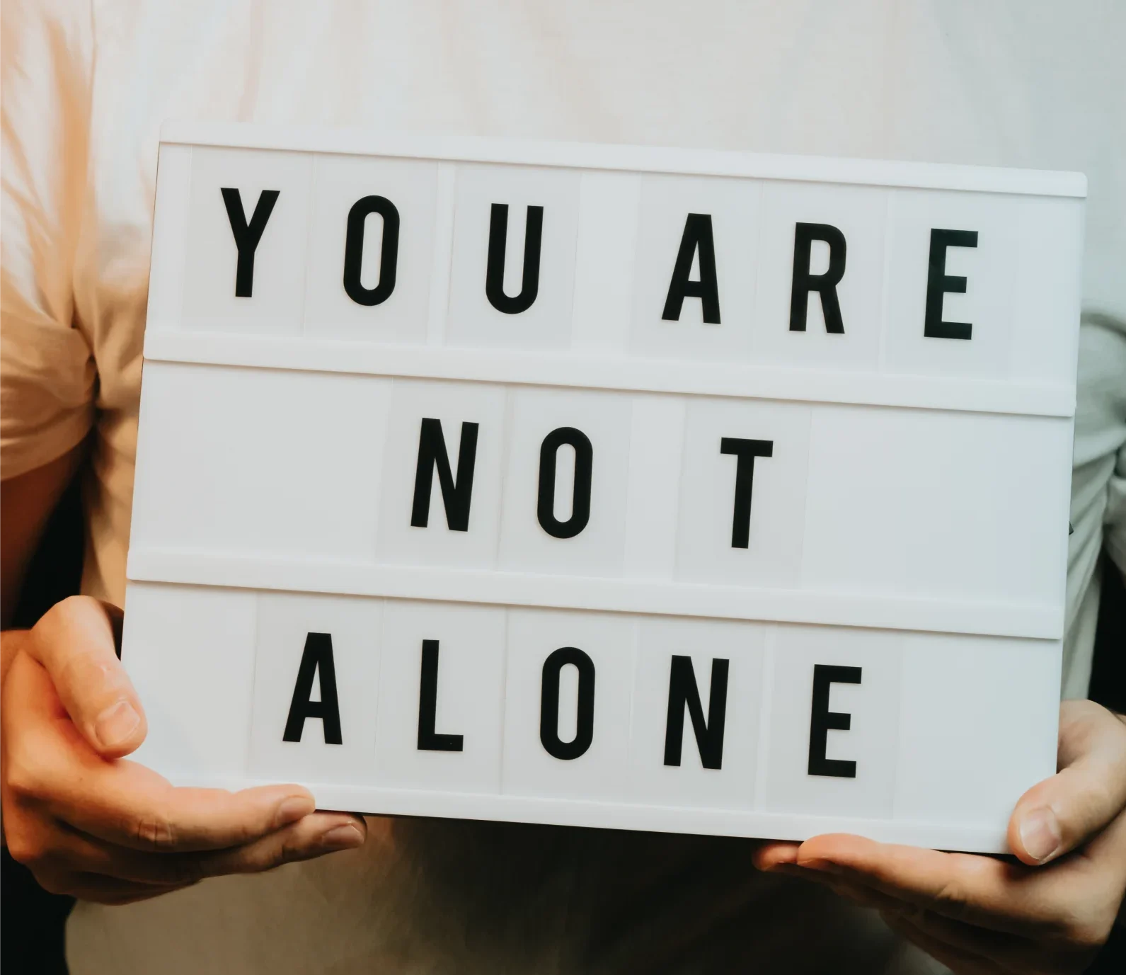 A person holding a sign that reads 'You Are Not Alone'.