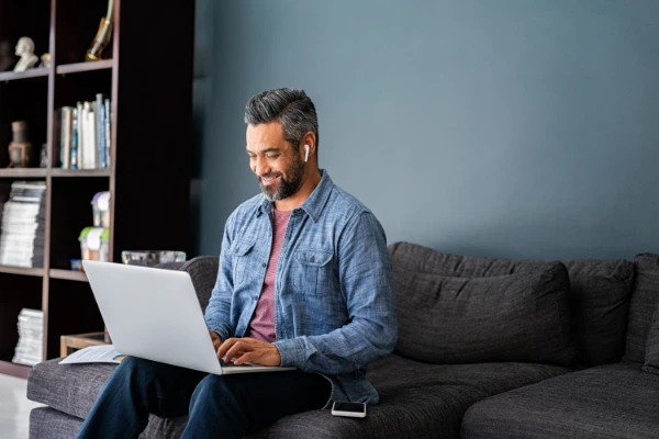 man sitting on a couch on his computer with an apple airpod in his ear