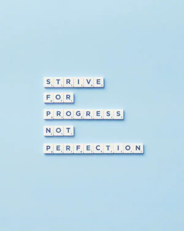 Scrabble tiles arranged on a light blue background spell out Strive for progress not perfection, with each word on a separate line—a motivational message often shared in ADHD counseling.