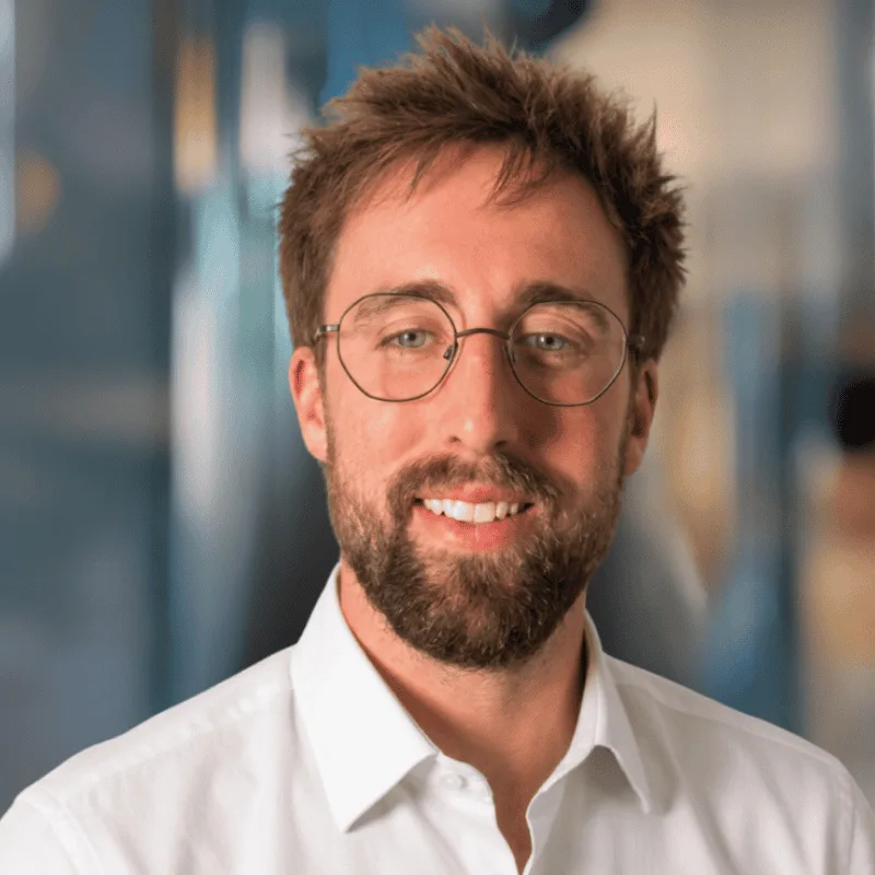 Wyatt Marr, Counseling Intern, Anchor of hope counseling in southlake texas, A man with light brown hair, a beard, and glasses smiles at the camera. He is wearing a white collared shirt and is positioned in front of a blurred blue and beige background.