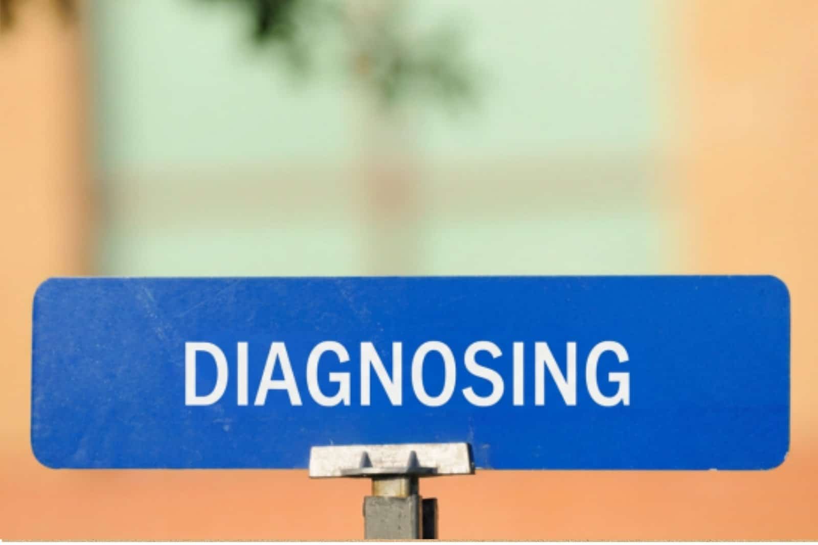 A blue sign with the word DIAGNOSING in bold white letters, mounted on a metal post, with a blurred background of orange and green tones.