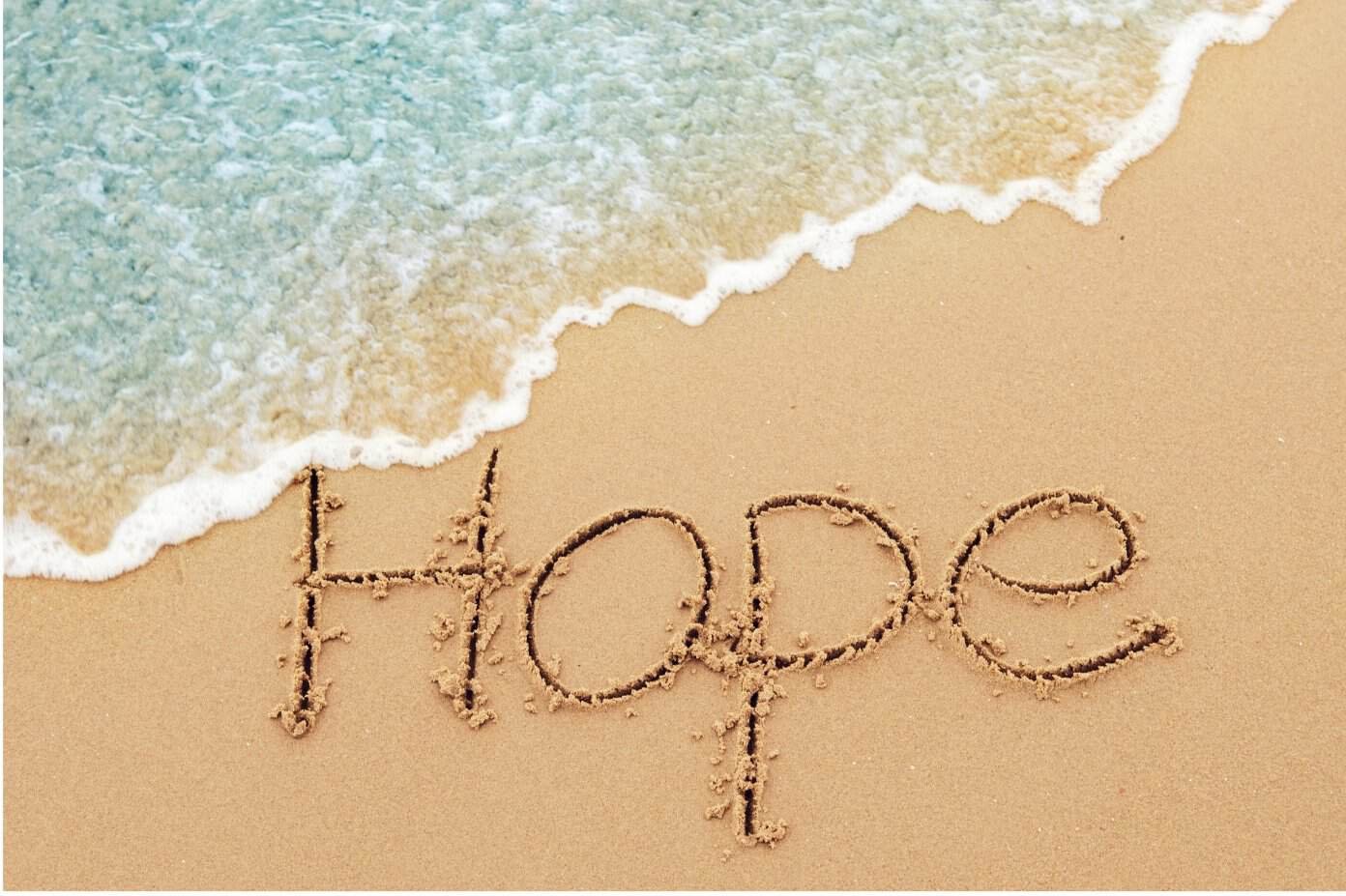 The word Hope is written in the sand near the shoreline, with a gentle wave approaching from the top left corner.
