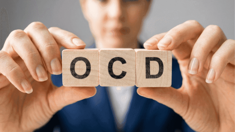 A person holds wooden blocks displaying the letters OCD toward the camera, with their face blurred in the background.