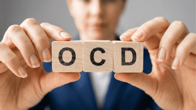 A person holds wooden blocks displaying the letters OCD toward the camera, with their face blurred in the background.